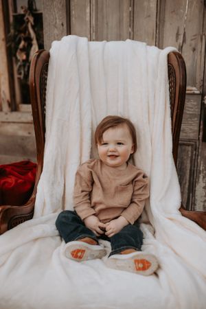 Sweet candid moments of a toddler sitting on white chair during photo session.