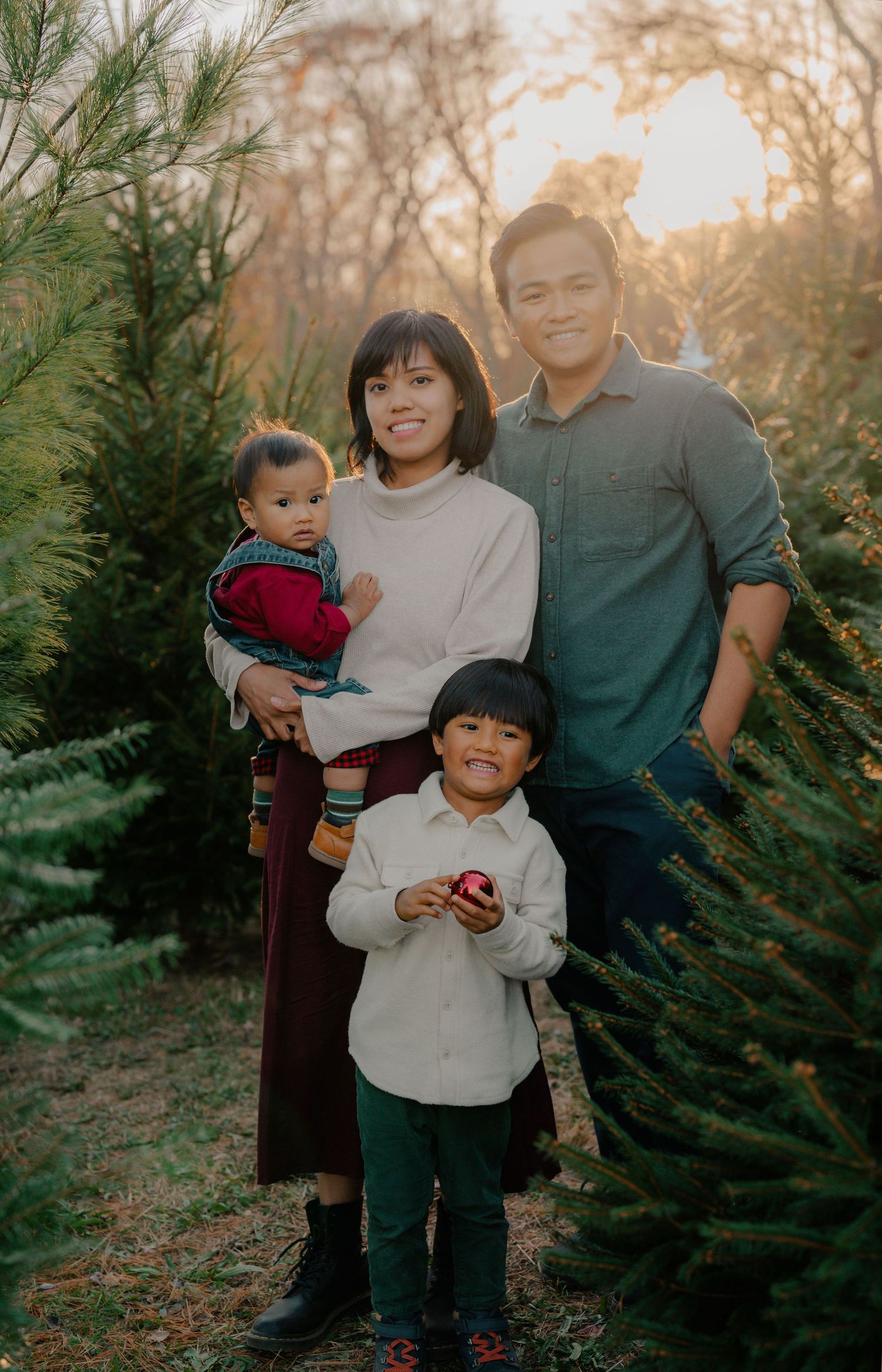 Family portrait among evergreen trees during golden hour with autumn colors in background.
