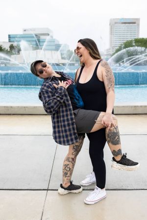 Playful couple having fun by a fountain with tattoos and casual clothing.