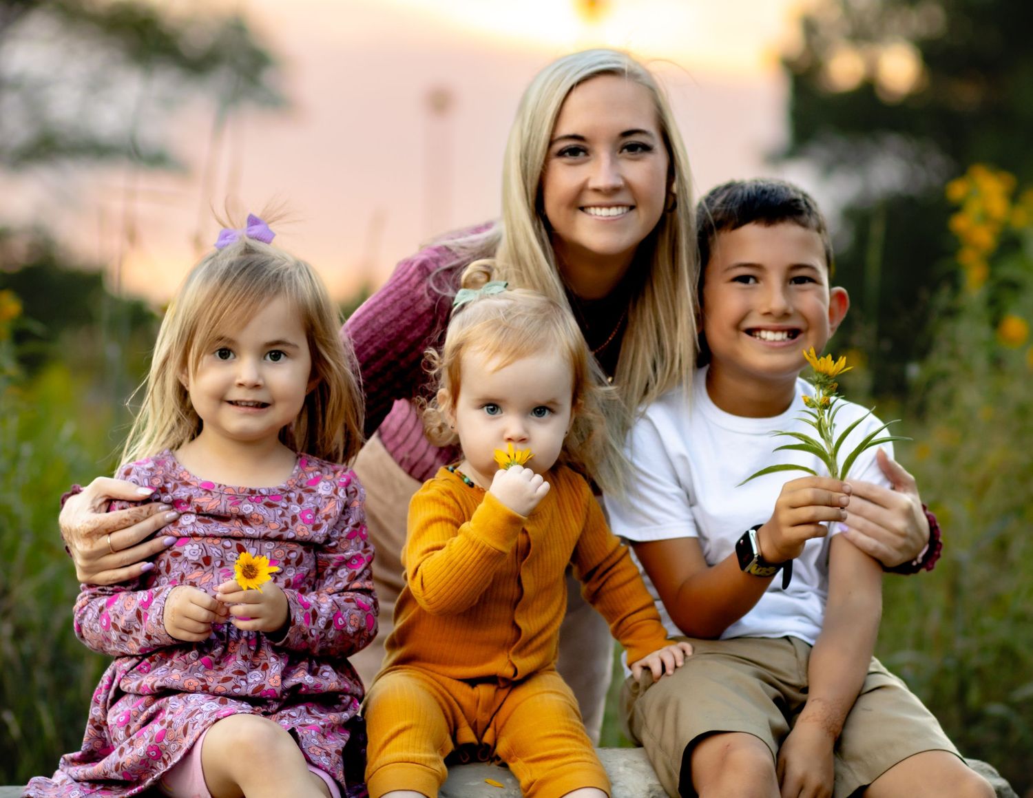 A family sits together outdoors during golden hour in a wildflower field, smiling and enjoying a warm summer evening.