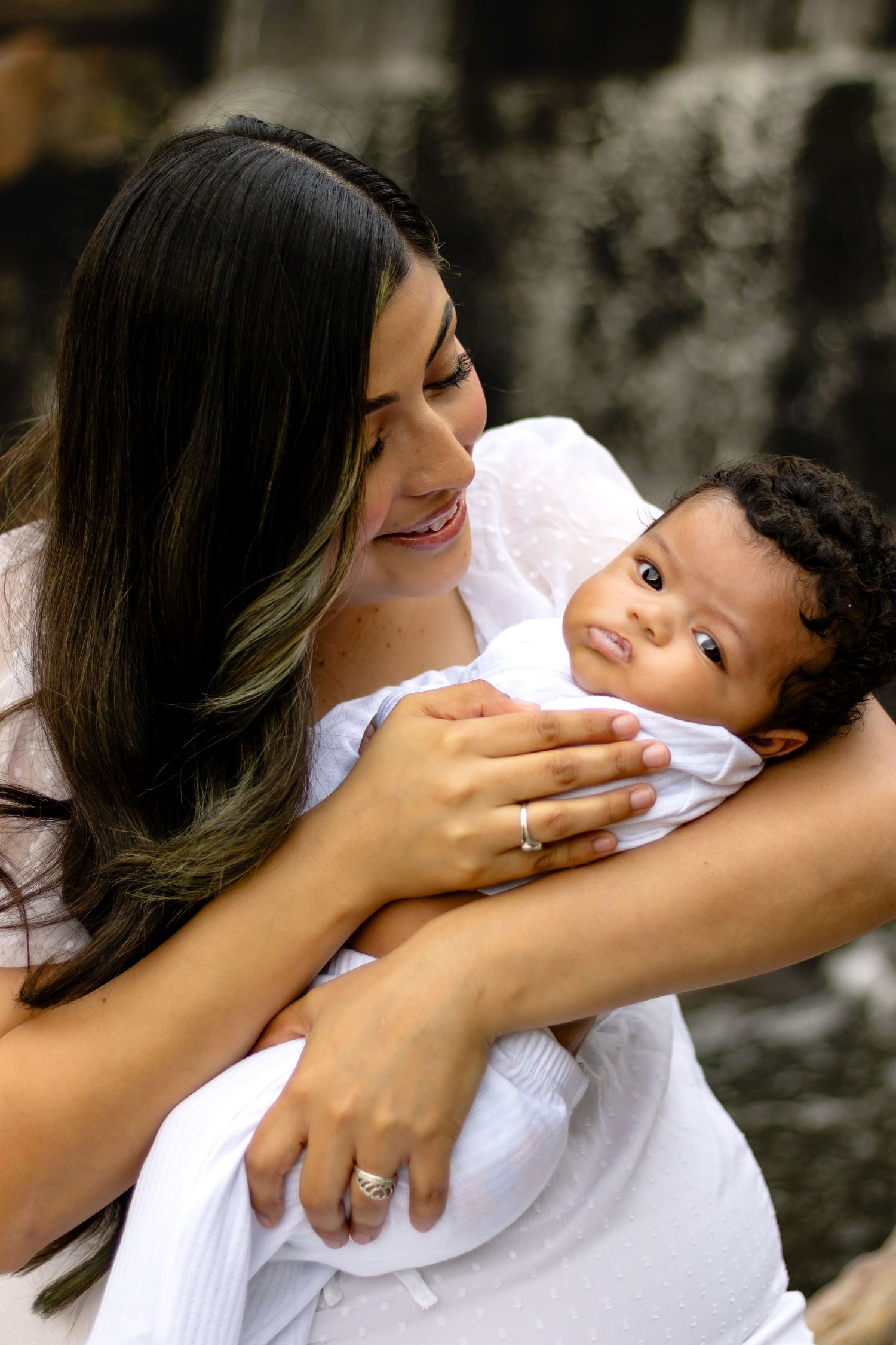 A tender moment between a mother and child dressed in white, sharing loving smiles against a natural background.