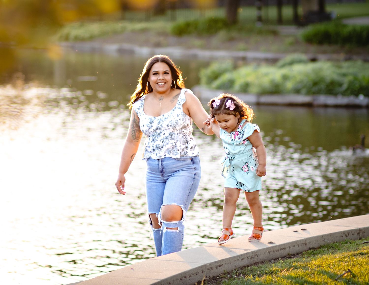 Two people walk hand in hand along a lakeside path during golden hour, creating joyful moments by the water.