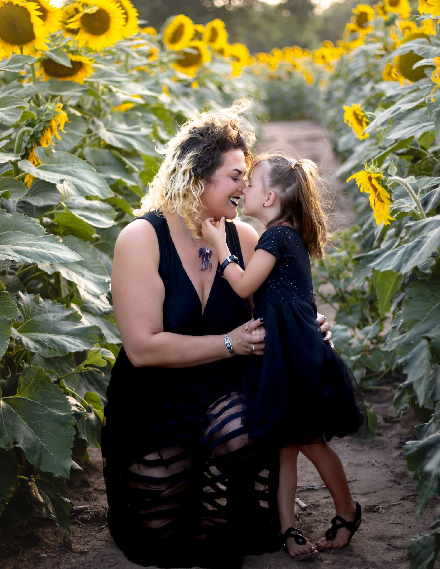 Two people share a joyful moment in a field of towering sunflowers during golden hour.
