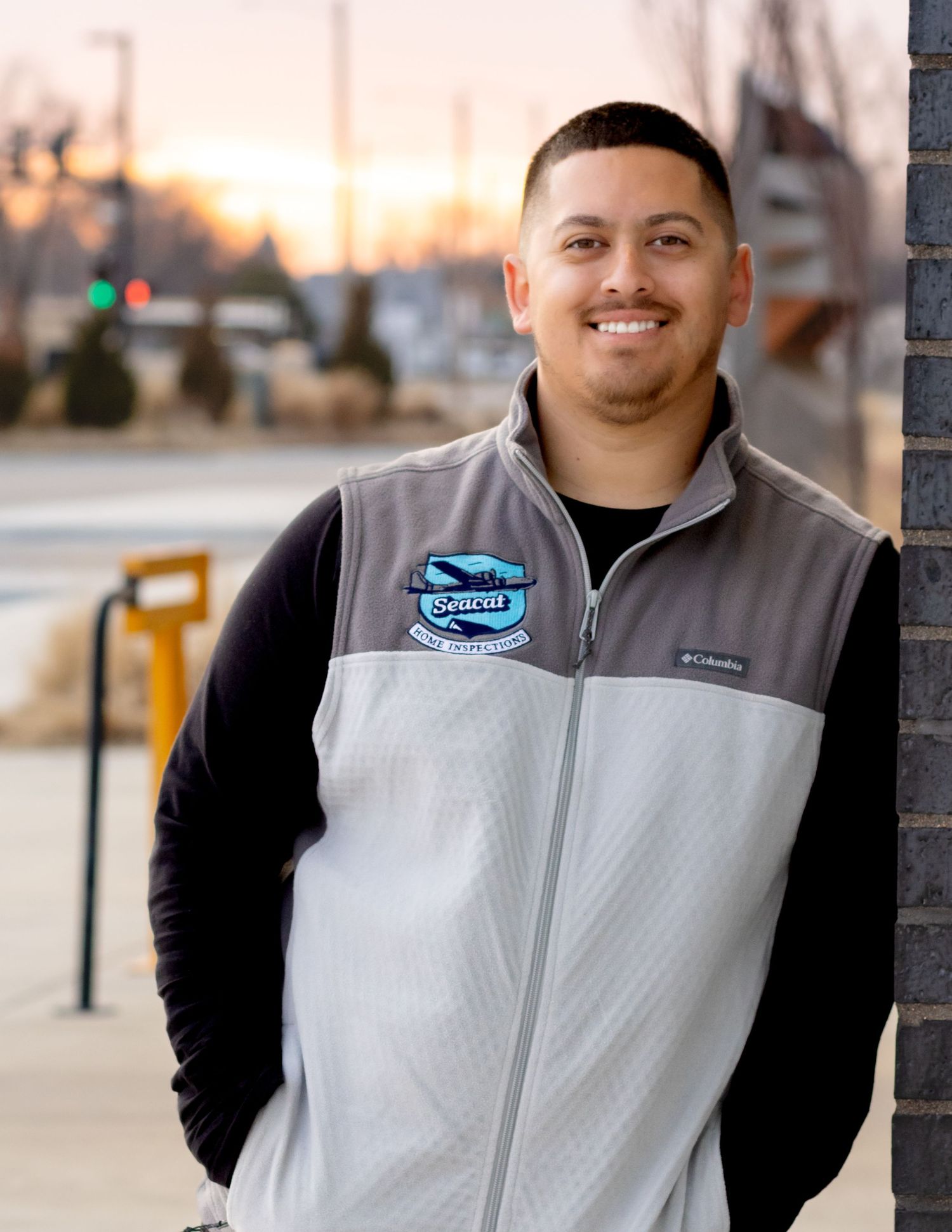 Person wearing a Columbia grey and white fleece vest smiles at camera during sunset in commercial setting.