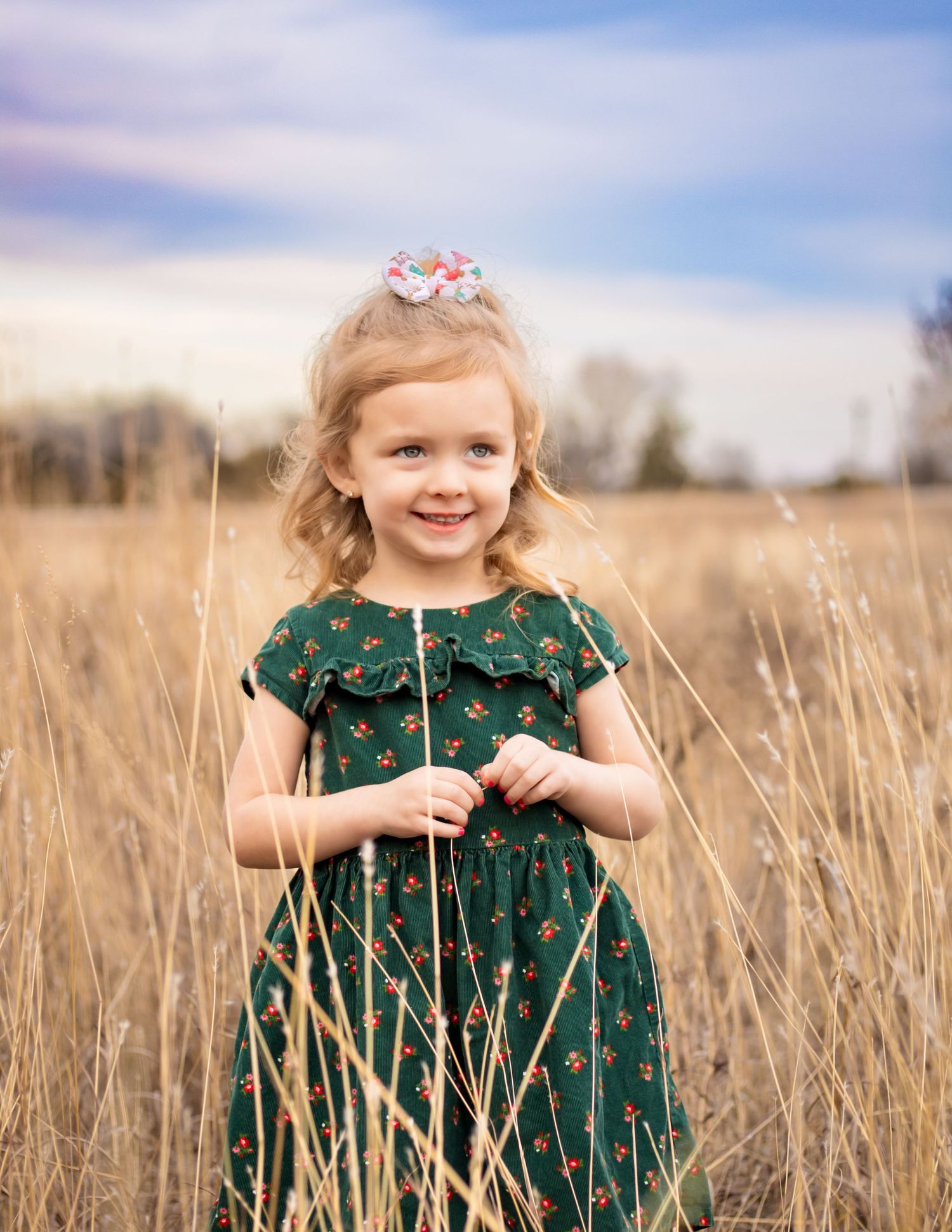 A joyful moment in a tall wheat field on a cloudy day features a green floral dress and a wildflower stem.