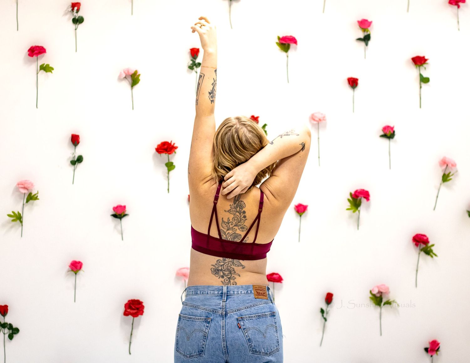 A figure in blue jeans and red crop top stands against a white wall decorated with scattered red roses.