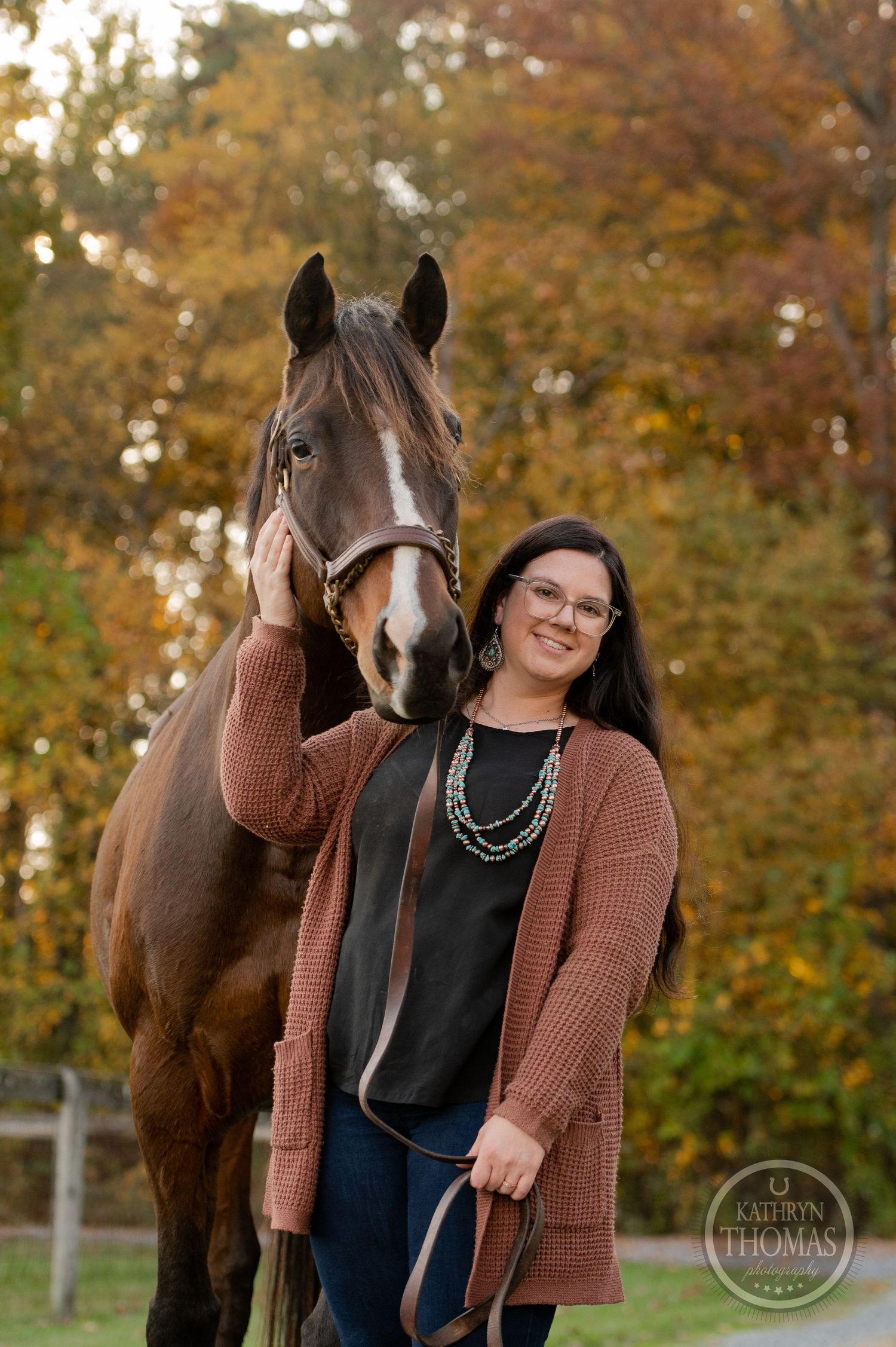 A bay horse and their companion pose together against vibrant fall foliage in the background.