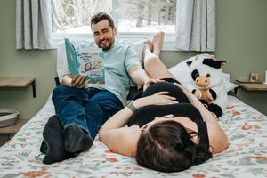 A couple relaxes on a bed reading to a woman's pregnant belly.