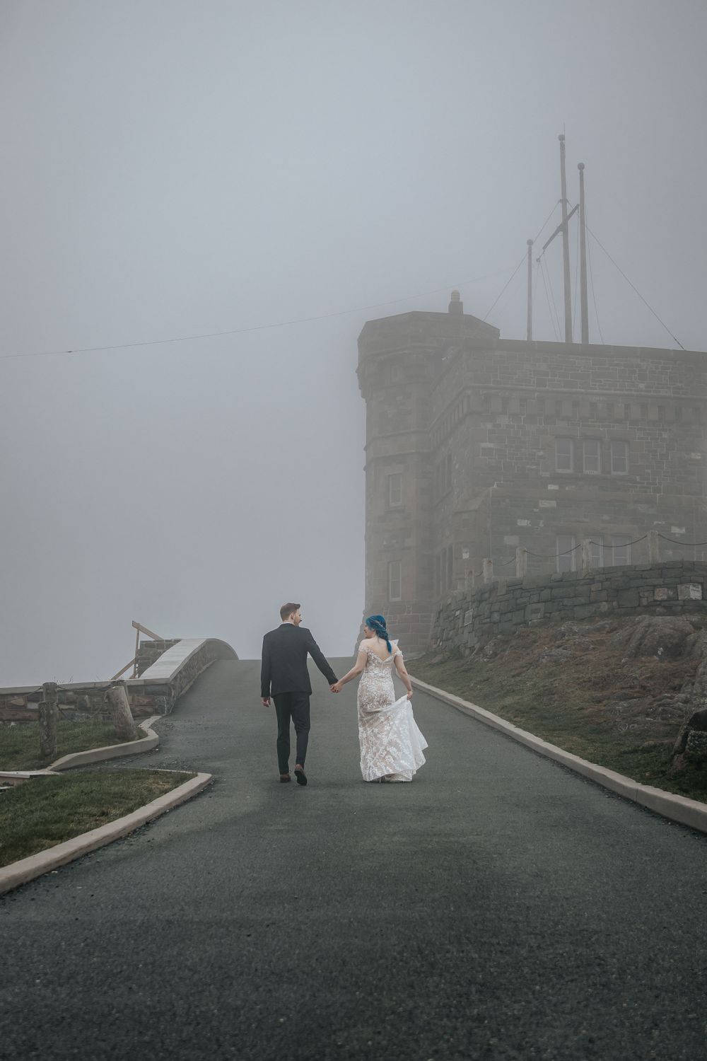 A couple walking on a misty road towards a stone castle on a foggy mountaintop.