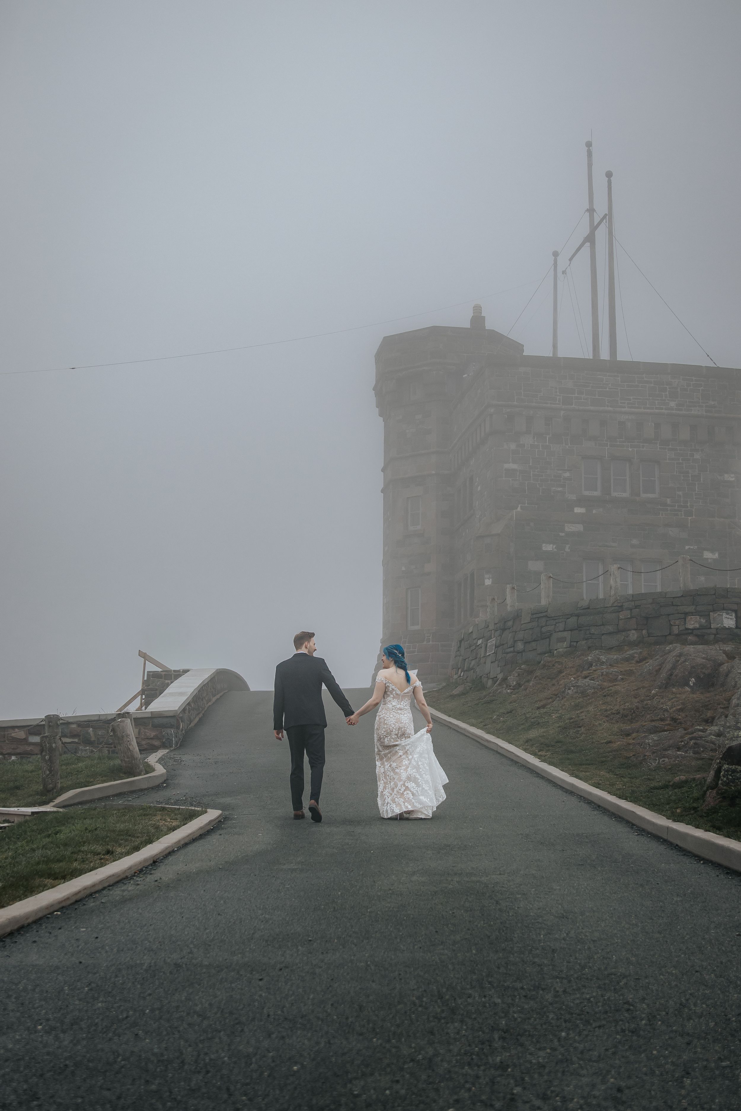 A couple walking on a misty road towards a stone castle on a foggy mountaintop.