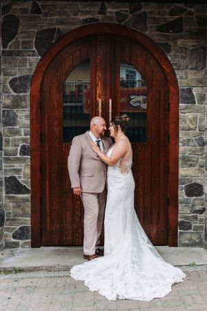 A couple shares an intimate moment in front of a beautiful arched wooden door with stone walls.