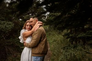 A couple embraces in a romantic woodland setting surrounded by lush greenery and natural light.