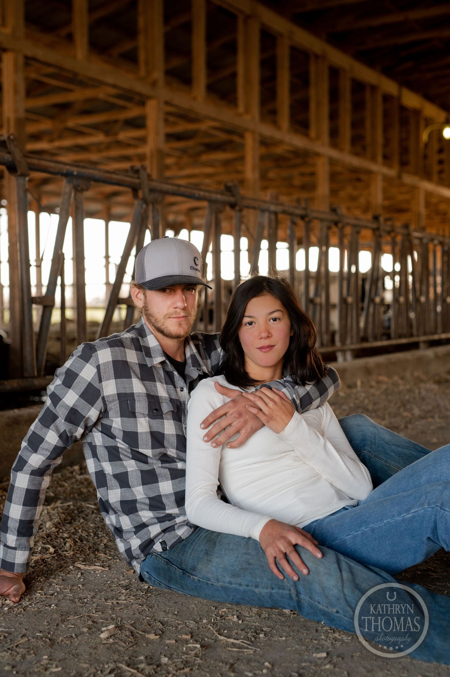A couple relaxes together under wooden barn beams during a rustic photoshoot on a farm.