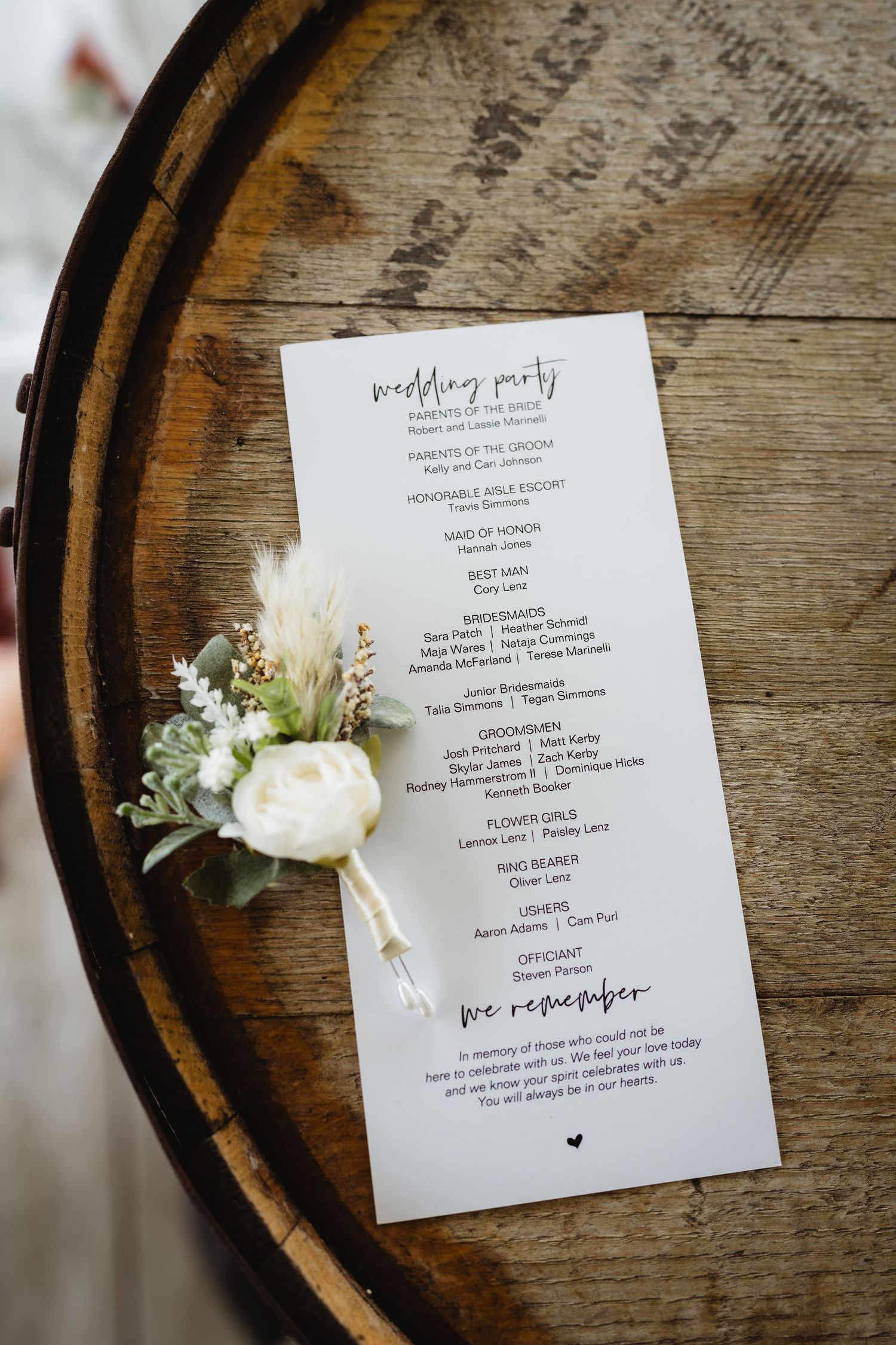 Elegant wedding program and white floral boutonniere arranged on rustic wooden barrel top.