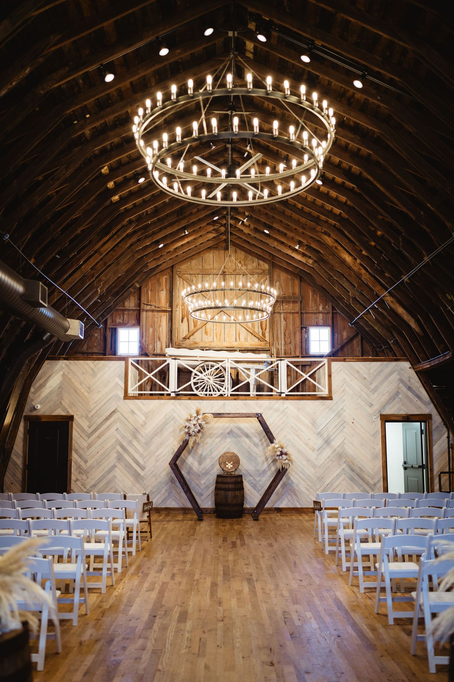 Beautiful rustic barn wedding venue interior with circular chandeliers and wooden beamed ceiling arranged for ceremony.
