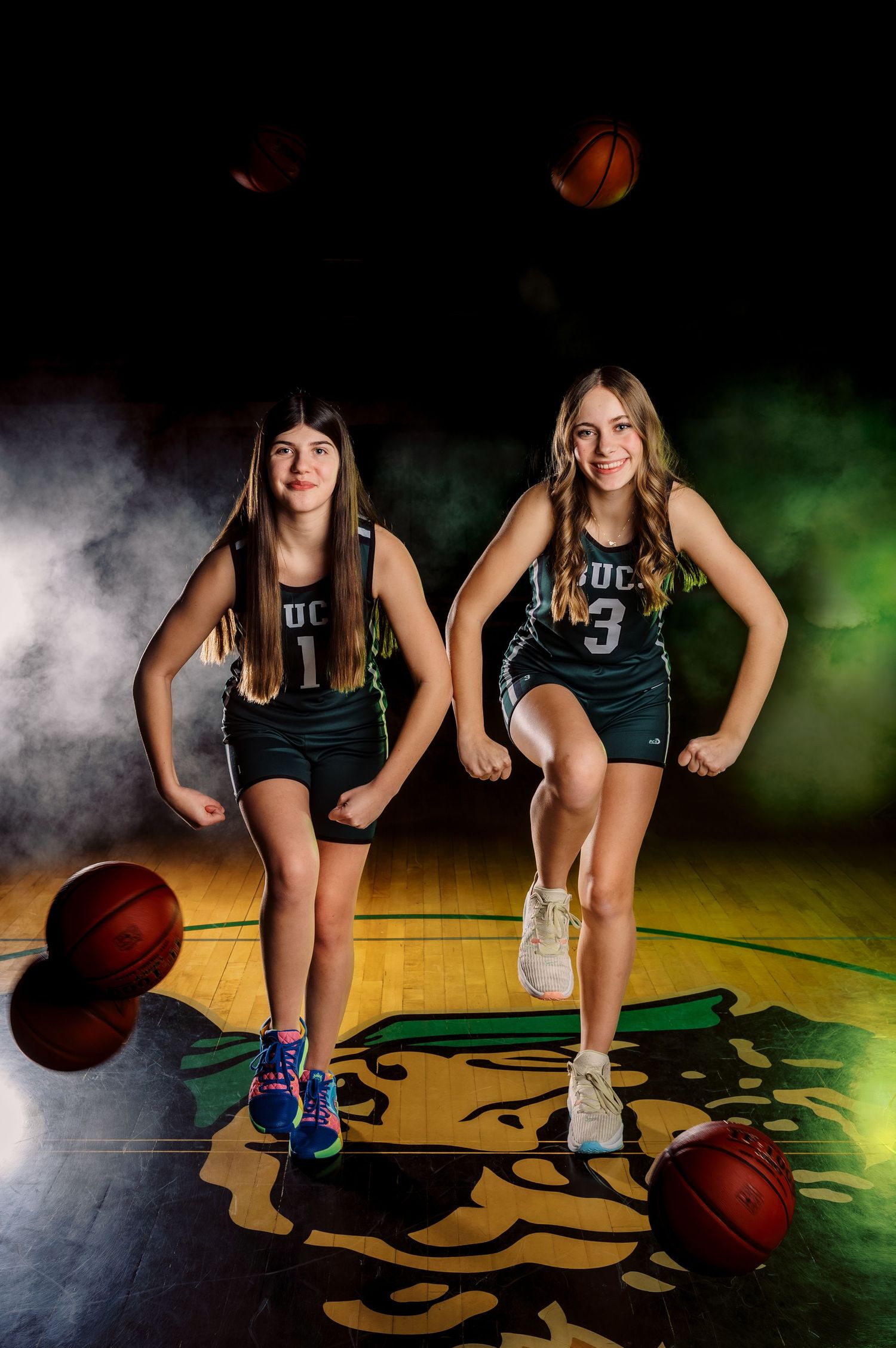 Young basketball player holding two basketballs against a dark background with dramatic smoke effects.
