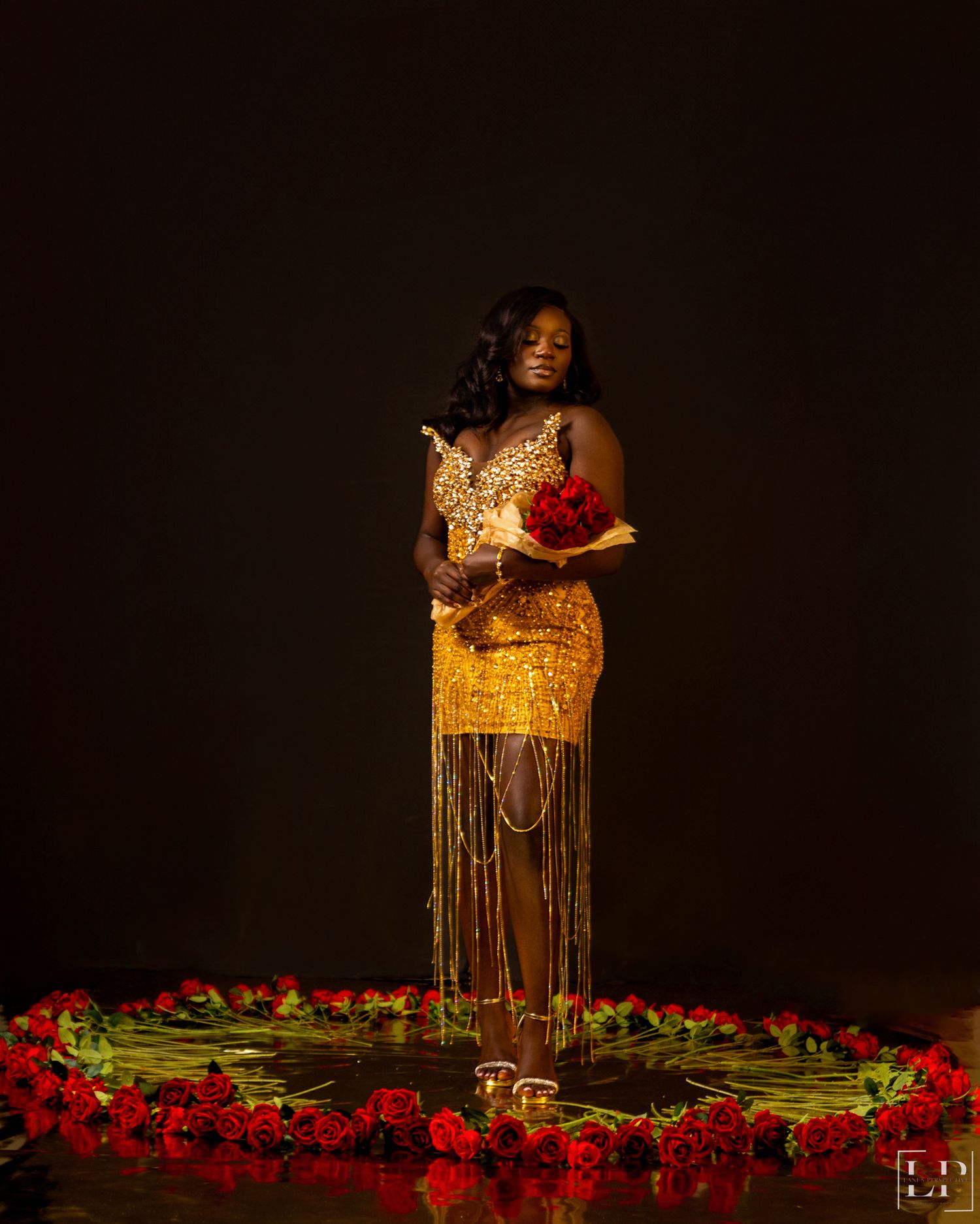 Dramatic portrait in gold sequined dress surrounded by red roses against black background.