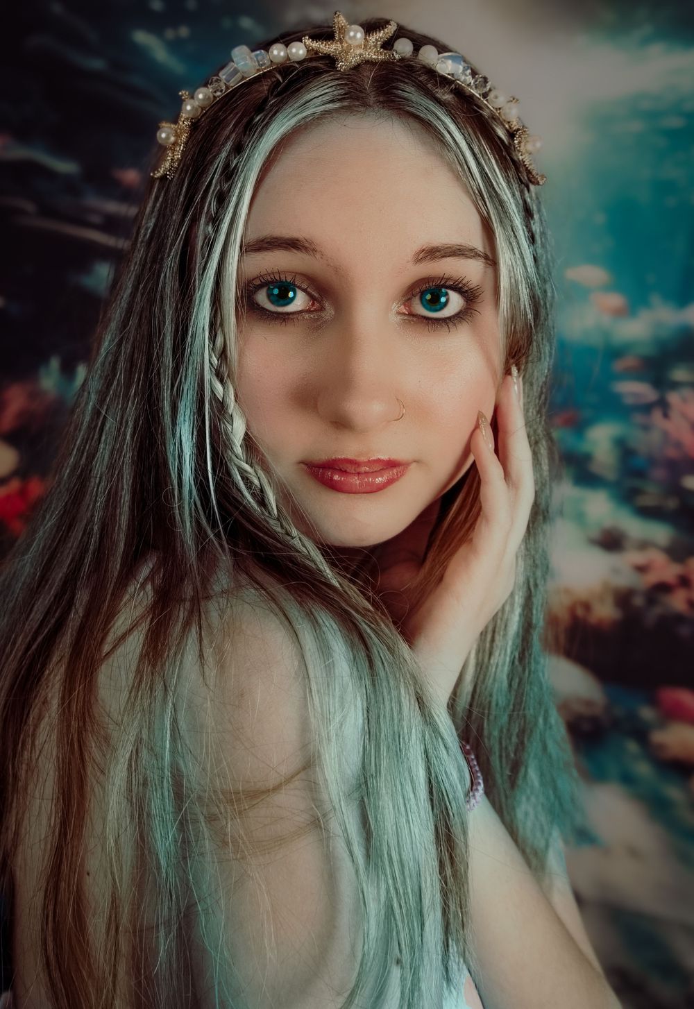 An ethereal portrait of someone with long teal-colored hair and blue eyes against a moody dark background.