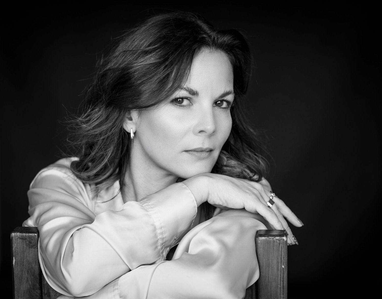 Eine schwarz weiß Serie einer Frau im Fotostudio fotografiert. Sie sitzt auf einem Stuhl und hat die Arme über die Lehne gelegt.