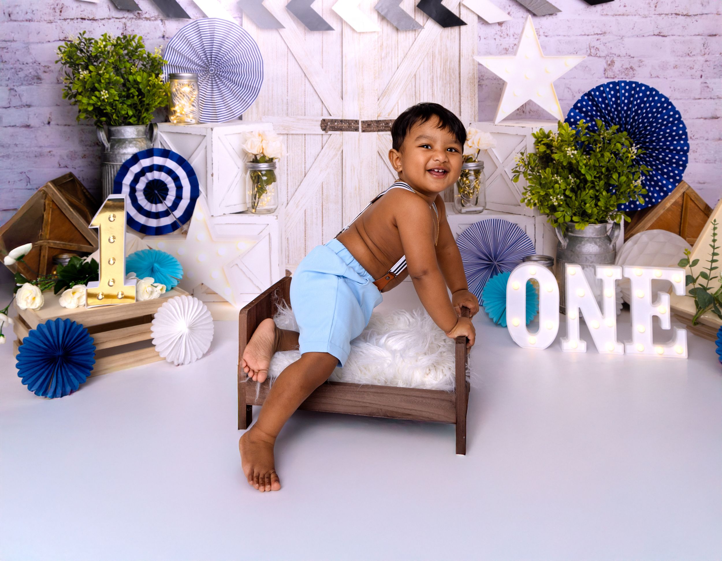 A collage of first birthday party photos with white and blue decorations shows a cake smash celebration setup.