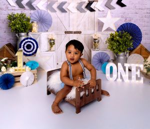 Baby wearing bear costume crawls playfully on wooden floor near white holiday decorations and paper fans.
