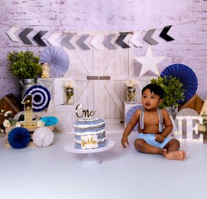 White and navy cake smash photo setup with paper fans, banners, and props for a first birthday celebration.