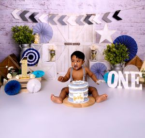 White brick backdrop with silver and black chevron banners and blue paper fans for cake smash photography session.
