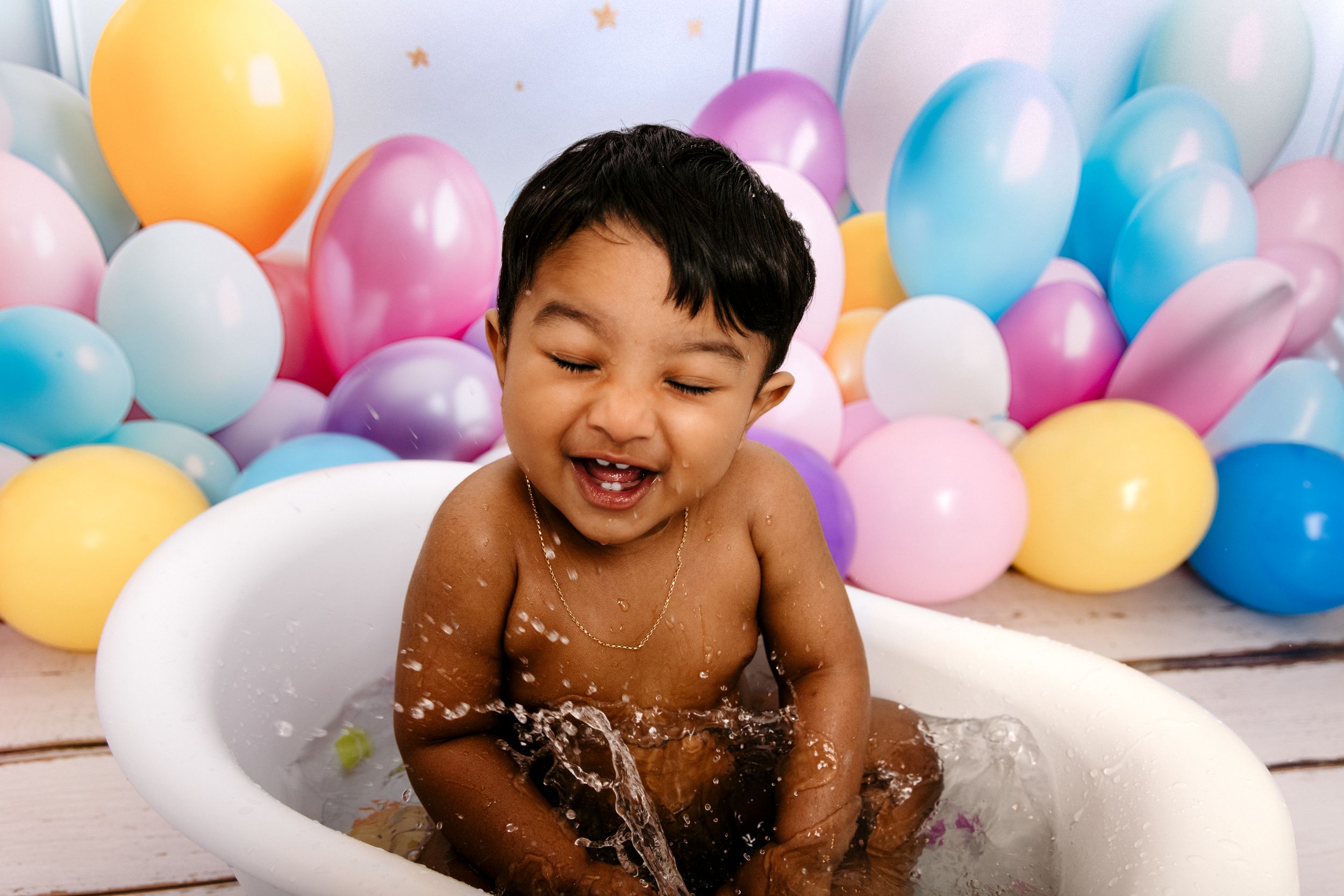 A joyful moment captured with colorful balloons in the background as someone plays with bubbles and water.