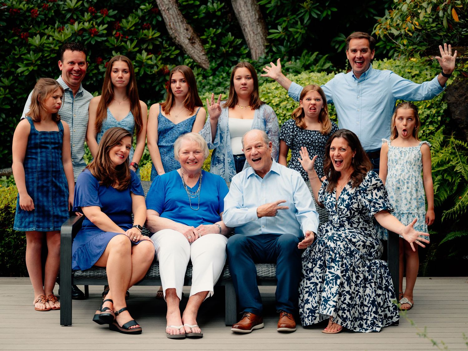 A group of people sitting casually on outdoor steps in coordinated blue and white outfits for a family photo shoot.