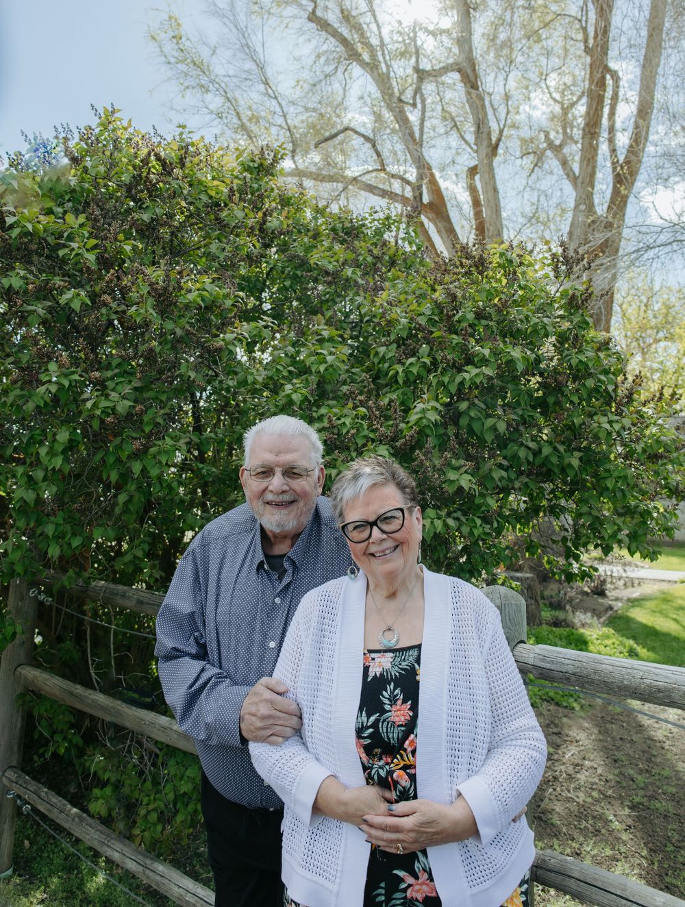 Couple sharing a tender moment together in front of green bushes on a sunny day.