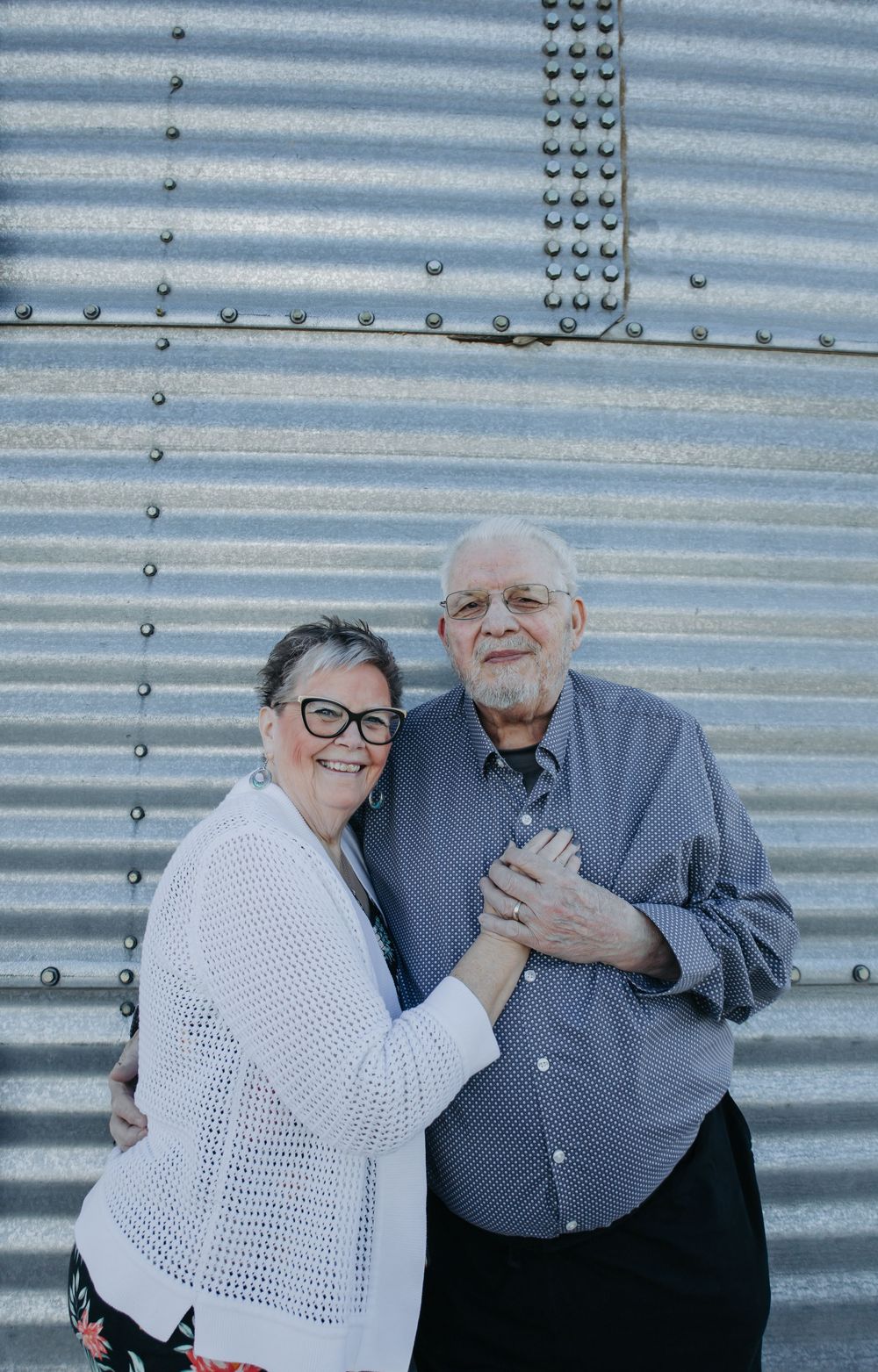 Couple embracing against a corrugated metal wall background showing affection.