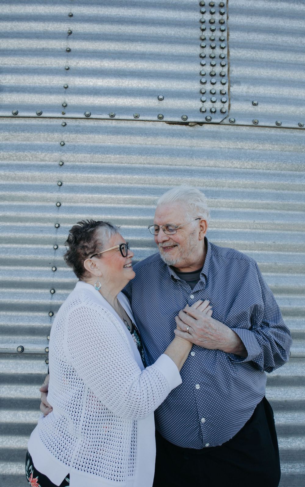 Loving couple sharing laughter while posing against industrial metal wall.