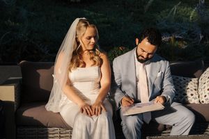 Newlyweds sign marriage documents together during outdoor wedding ceremony in elegant formal attire.