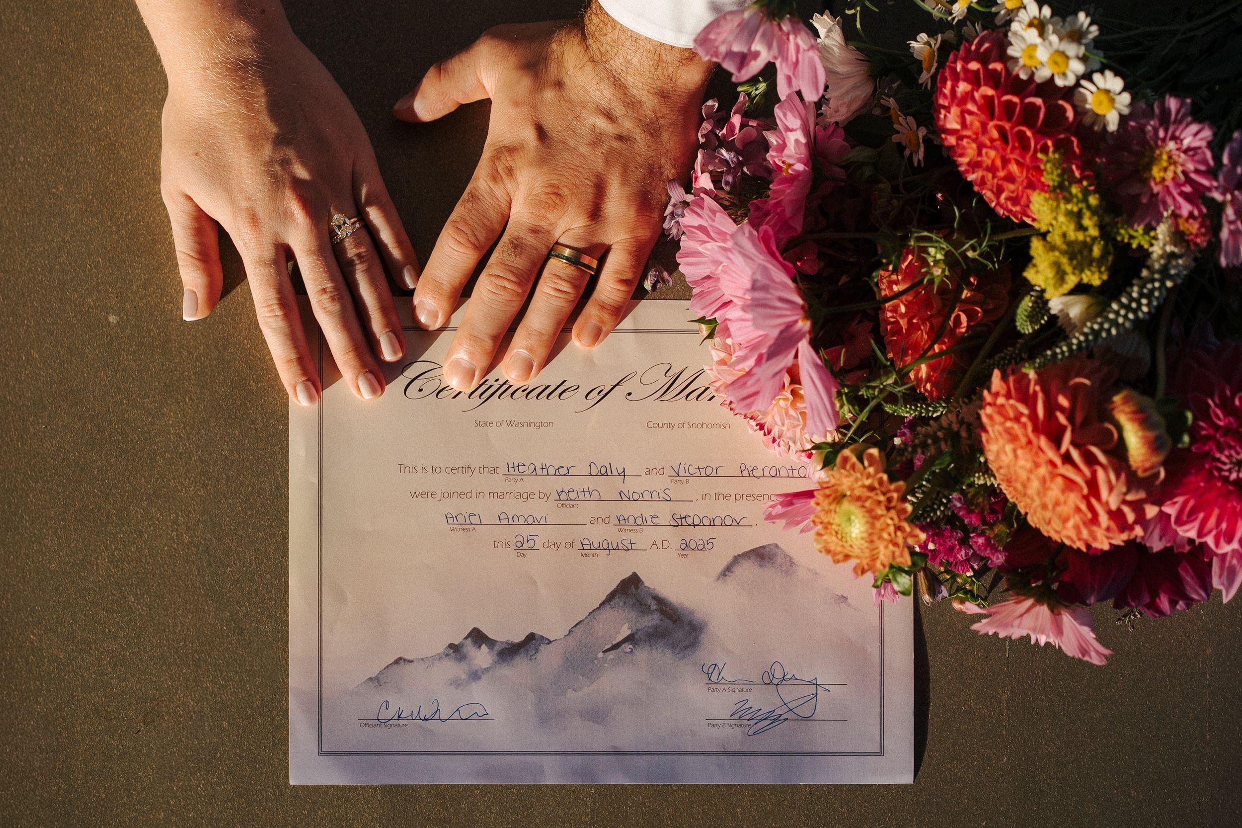 Marriage license signing with bright florals and hands shown holding a pen against the document paper.