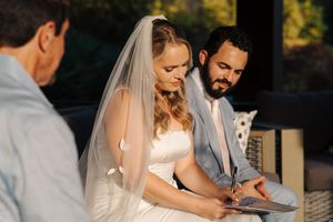A couple signs marriage documents at their outdoor wedding ceremony while wearing formal attire.