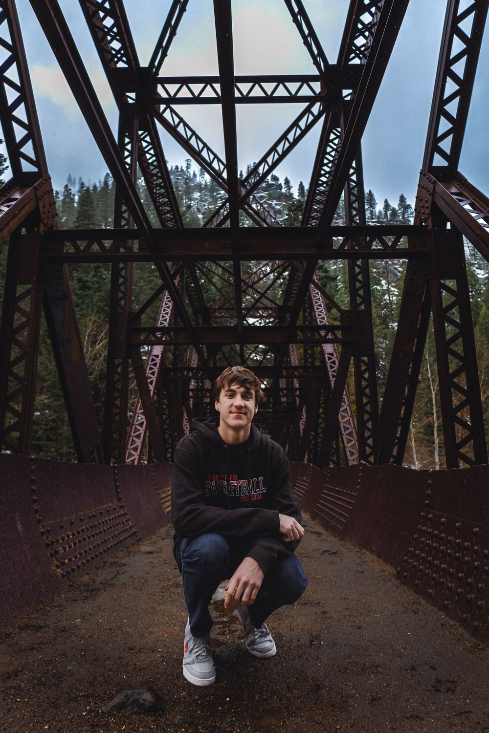 An old rustic railroad bridge spans across a scenic forest setting on a cloudy day.
