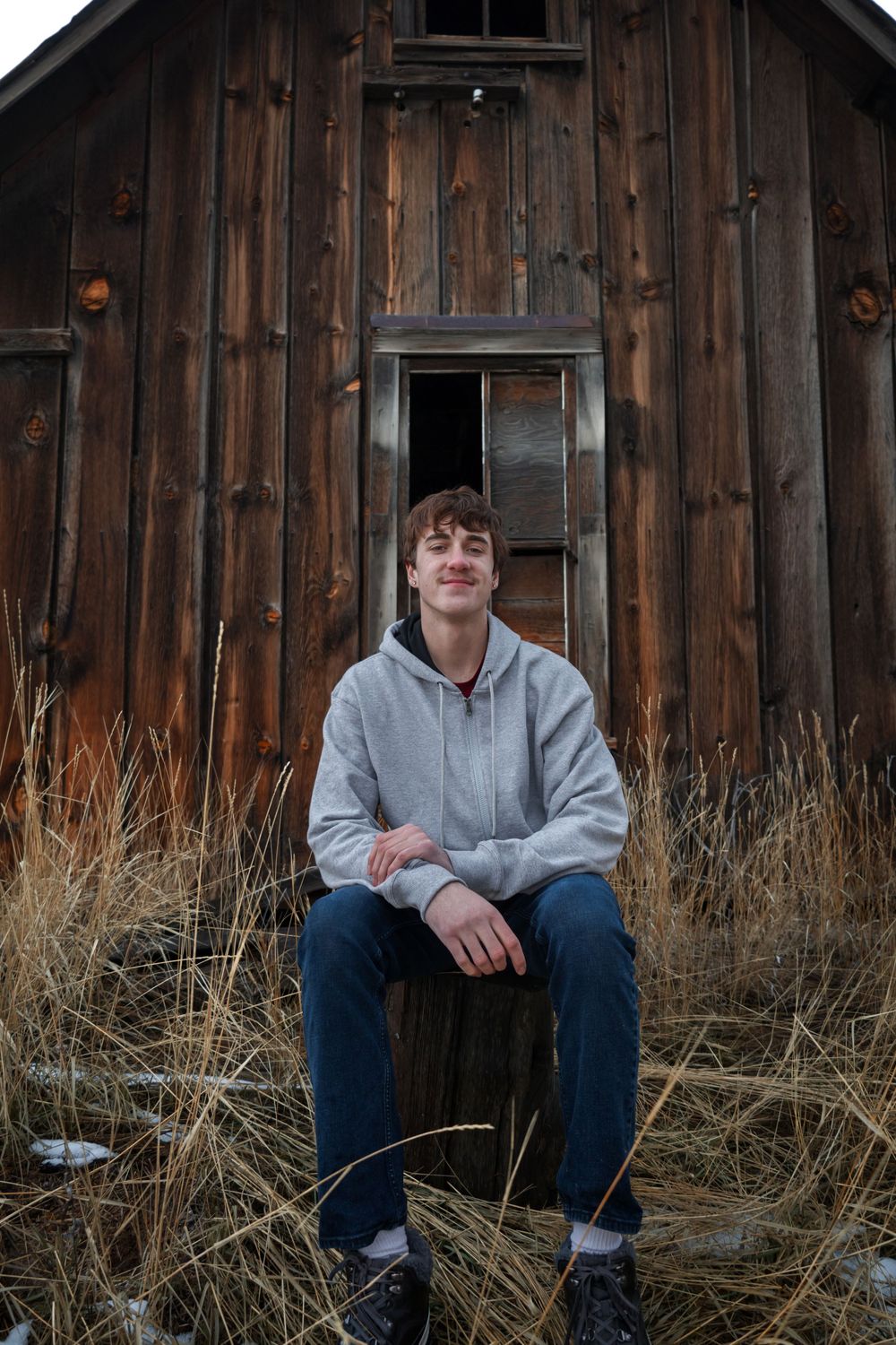 A rustic wooden cabin with vertical weathered boards surrounded by winter grass.