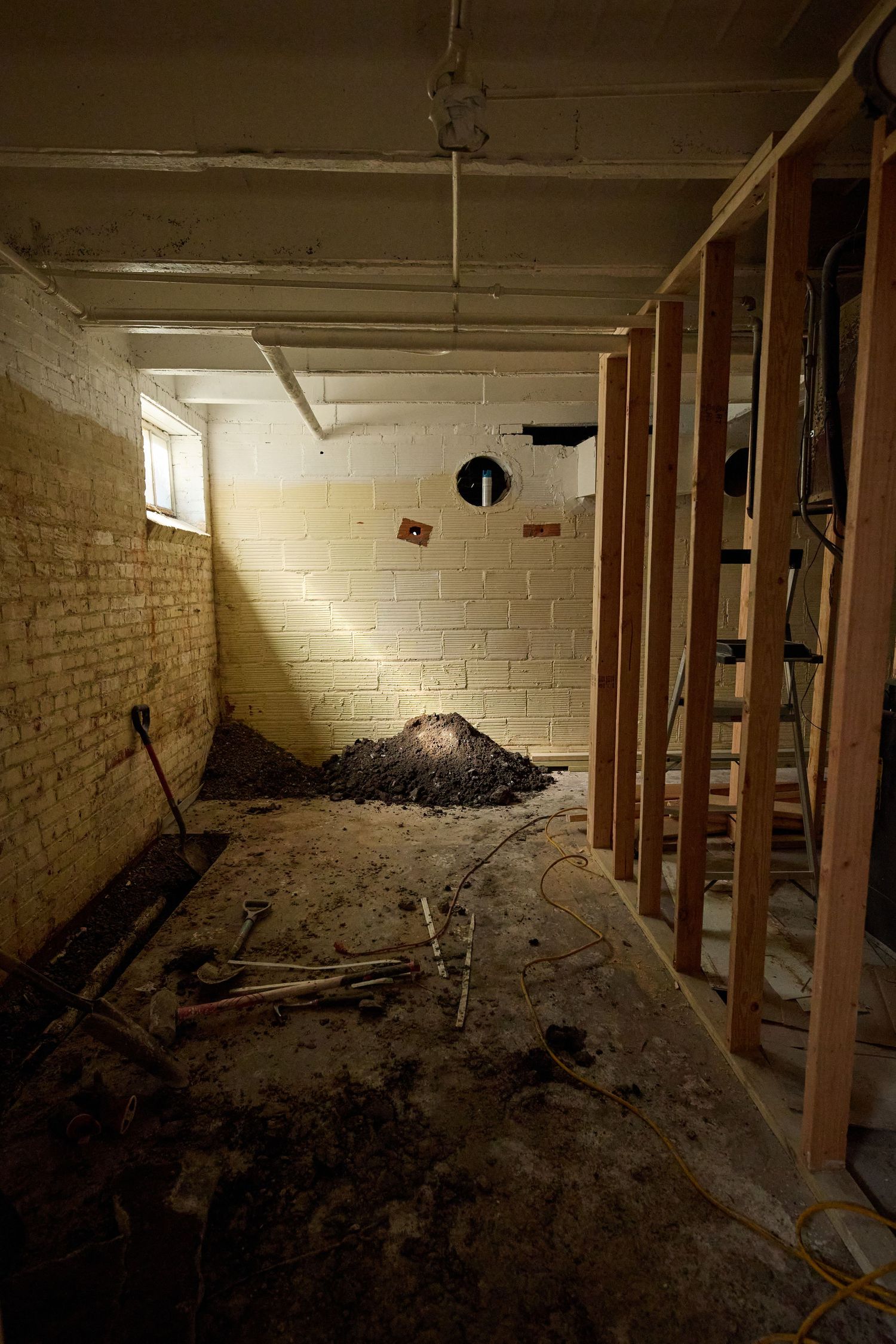 Unfinished basement room with dirt piles, exposed wooden studs, and painted concrete block walls.