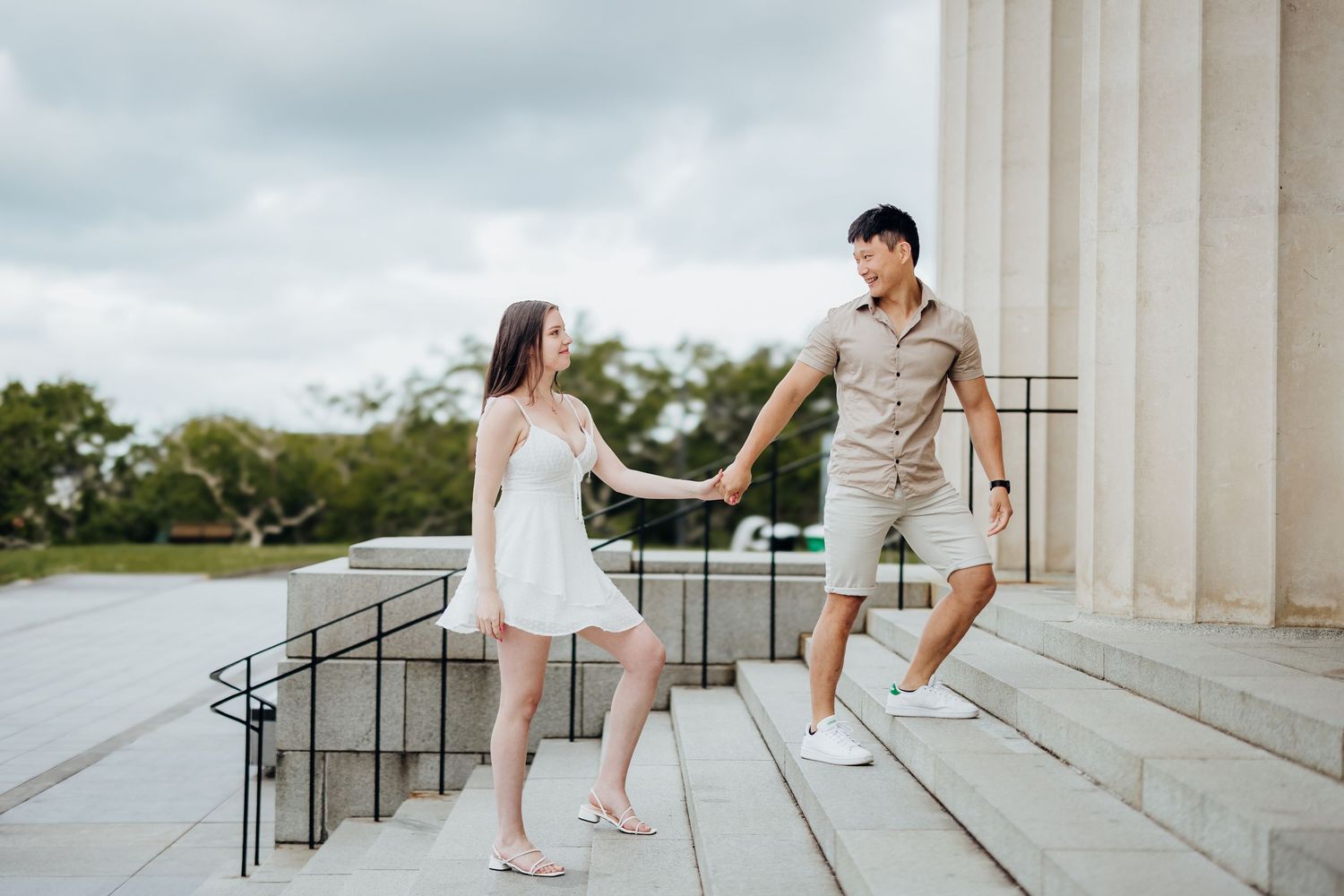 Couple sitting playfully on white stone steps at Jefferson Memorial during engagement photography session.