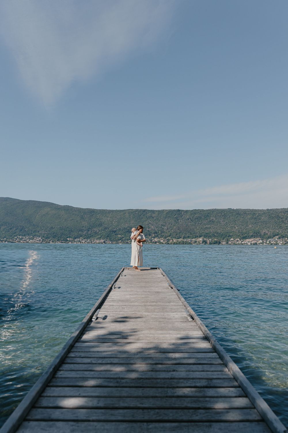 Une maman avec son bébé au bord du lac d'Annecy sur un ponton lors d'une séance photo famille.