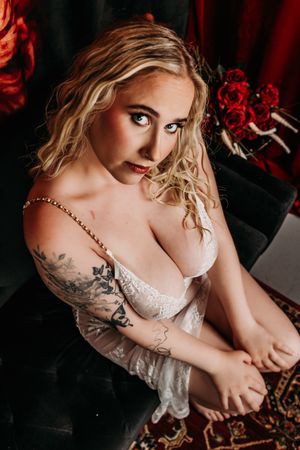 Intimate boudoir portrait featuring lace lingerie, blonde wavy hair, and floral tattoo art in a dramatic red setting. Grand Rapids Boudoir S