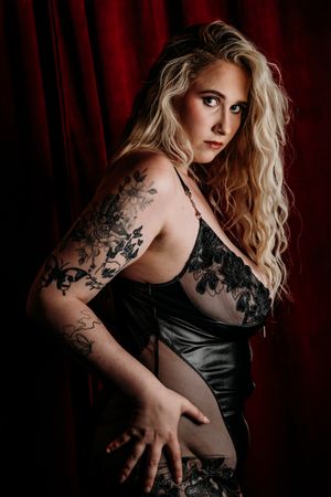 Artistic portrait with dramatic lighting shows intricate floral tattoo designs against black sheer fabric and dark background. Grand Rapids