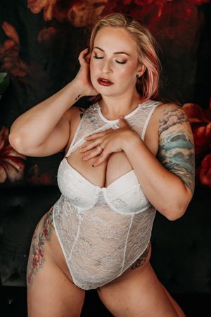 Boudoir photography of woman in white lace lingerie on dark background with dramatic red lighting. Grand Rapids Boudoir Photography