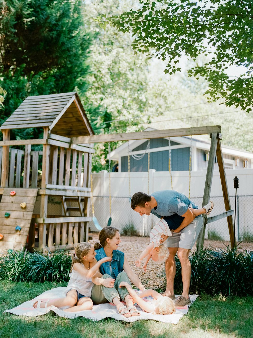 Family enjoying outdoor playtime near a backyard wooden playhouse and swing set.
