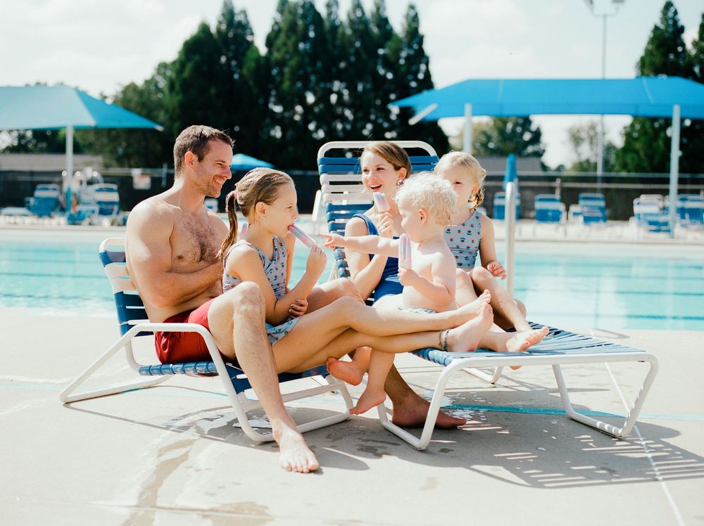 Group relaxing on lounge chairs by community swimming pool on sunny day.