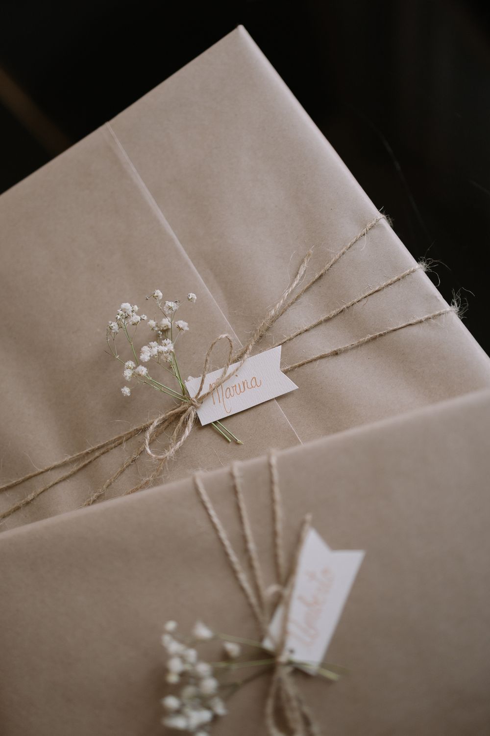Elegantly wrapped kraft paper packages tied with twine and decorated with delicate baby's breath flowers and name tags.