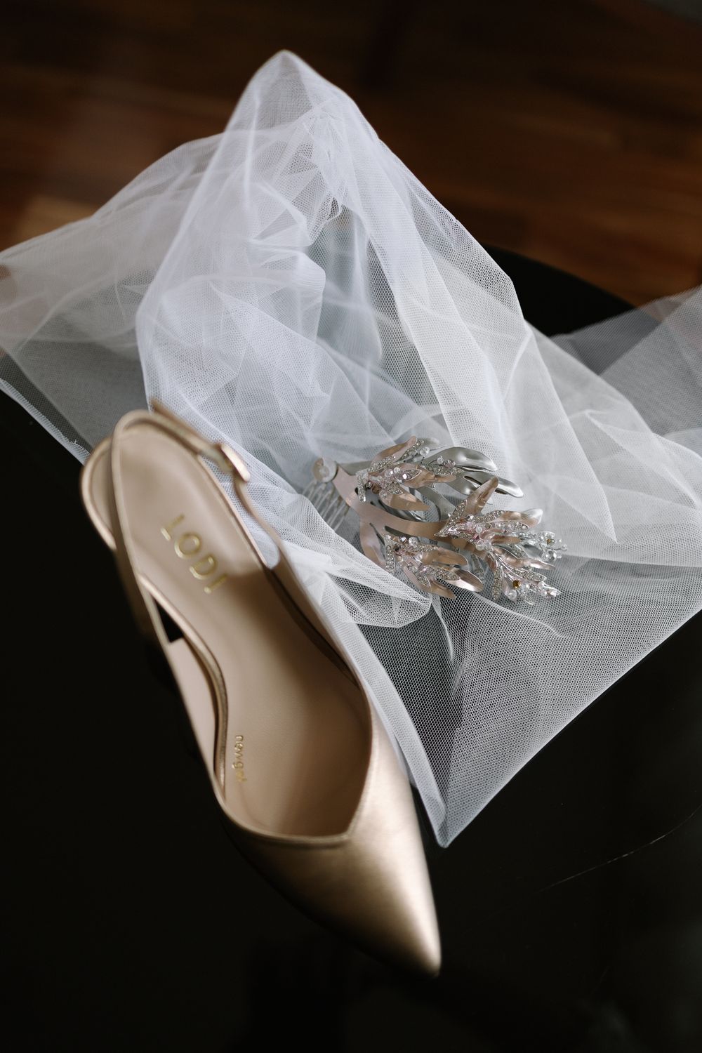 Elegant cream-colored bridal shoe with delicate veil and crystal accessories on dark wooden surface.