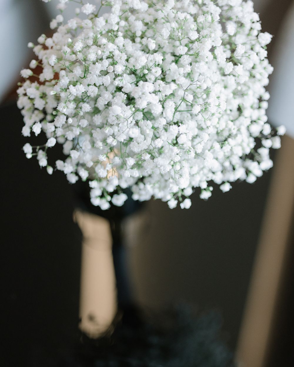 A delicate bouquet of white baby's breath flowers with soft green foliage wrapped in dark ribbon.