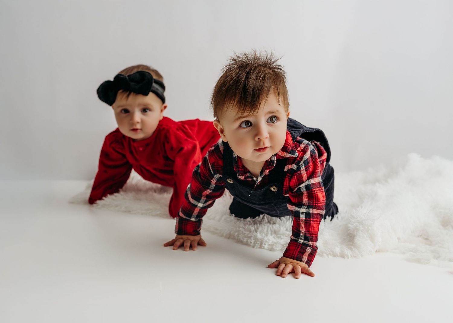 A young child wearing a red plaid shirt lies on a white backdrop in a crawling pose creating a playful photoshoot scene.