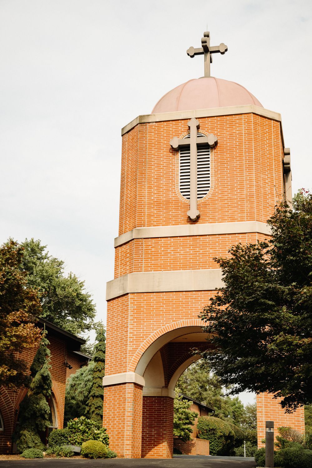 Modern brick church entrance with arched doorway and dome topped with cross in daylight.
